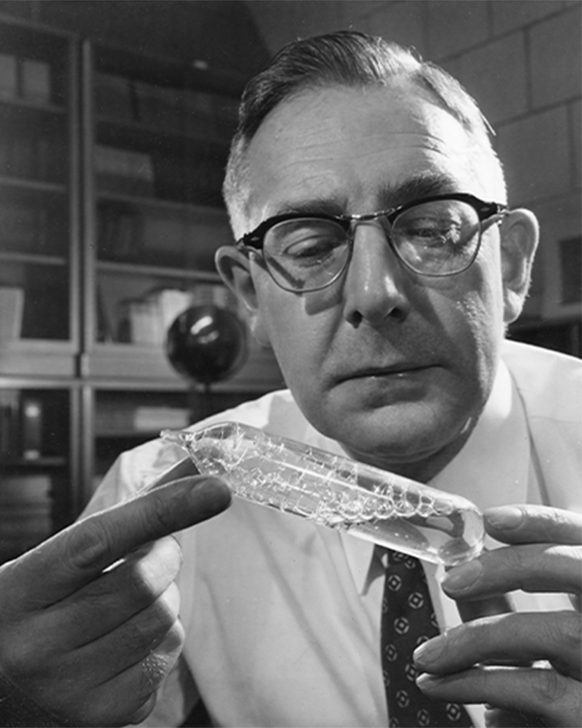 A portrait of Cyril Smith examining a glass tube filled with clear liquid in his hands.